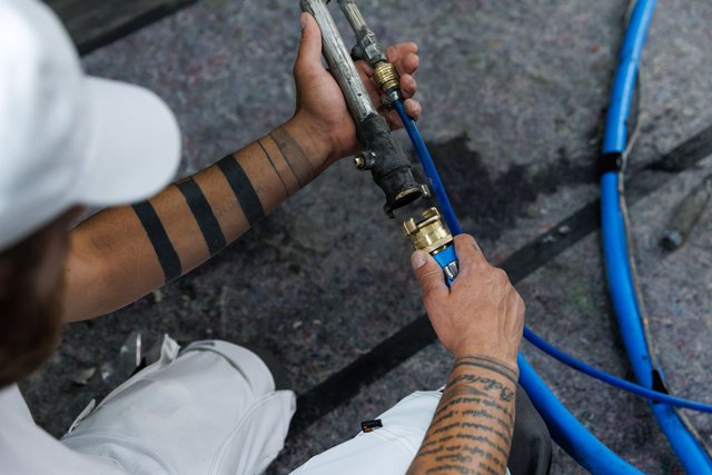 Arbeiter verbindet blaue Schläuche mit Metallkupplung, Nahaufnahme