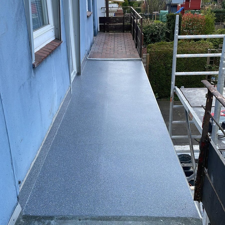 Balkon mit frischer grauer Beschichtung, daneben Baugeruest am Haus
