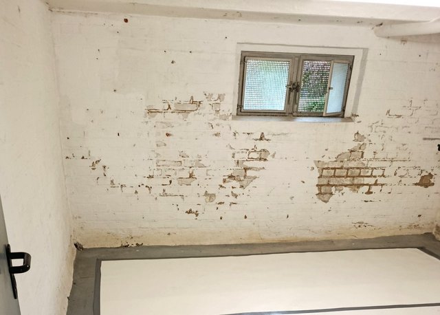 Abgeplatzte Kellerwand mit freiliegendem Mauerwerk unter kleinem Fenster