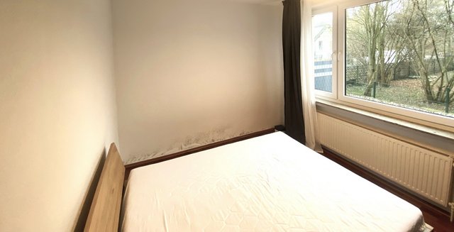 Schimmelflecken am unteren Wandbereich neben Bett im Zimmer