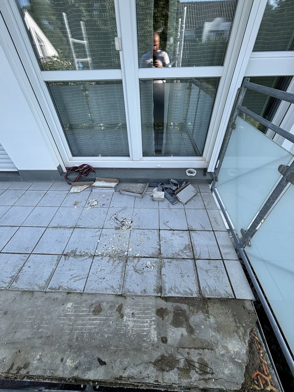 Beschädigte Balkonfliesen vor Terrassentür, Bauschutt und freigelegte Betonfläche