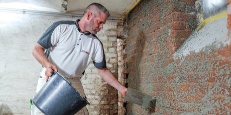 ISOTEC worker applies grey compound to brick wall.
