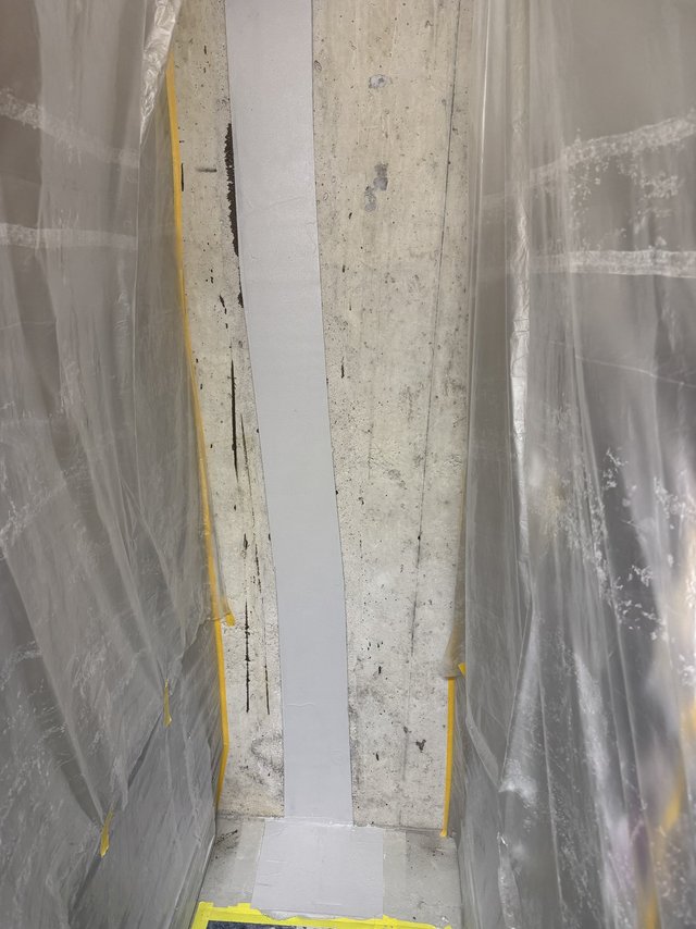 Grauer Dichtungsstreifen auf Betonwand, seitlich mit Schutzfolie abgeklebt