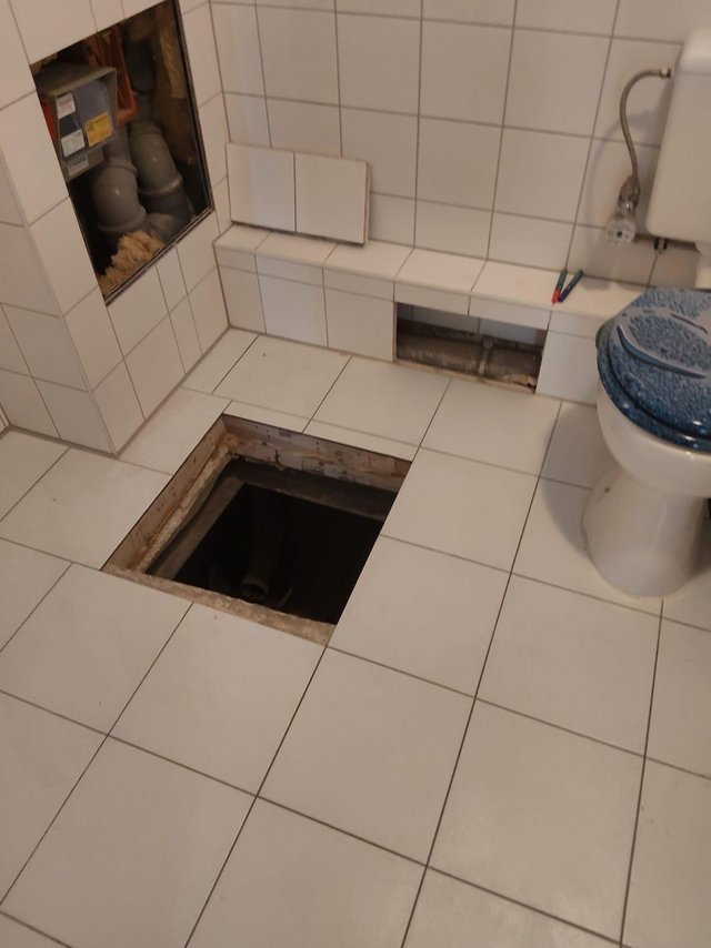 Geoeffneter Fliesenboden im Bad mit freigelegtem Schacht und sichtbaren Rohren