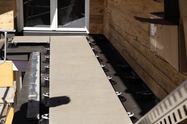 Beige Großformatplatten liegen auf schwarzen Stelzlagern an Balkon.