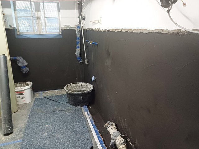 Schwarze Masse auf Wand aufgetragen, Rohre mit blauem Klebeband abgedeckt