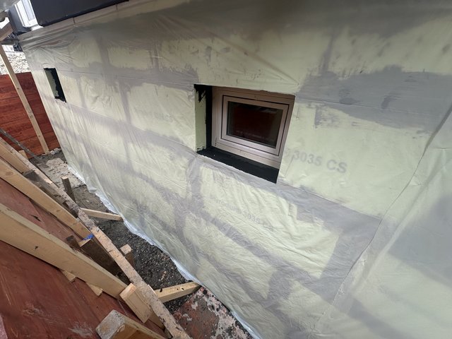 Schwarze Masse um Kellerfenster auf abgedeckter Außenwand aufgetragen