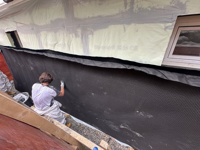 Arbeiter befestigt schwarze Noppenbahn an freigelegter Kellerwand.