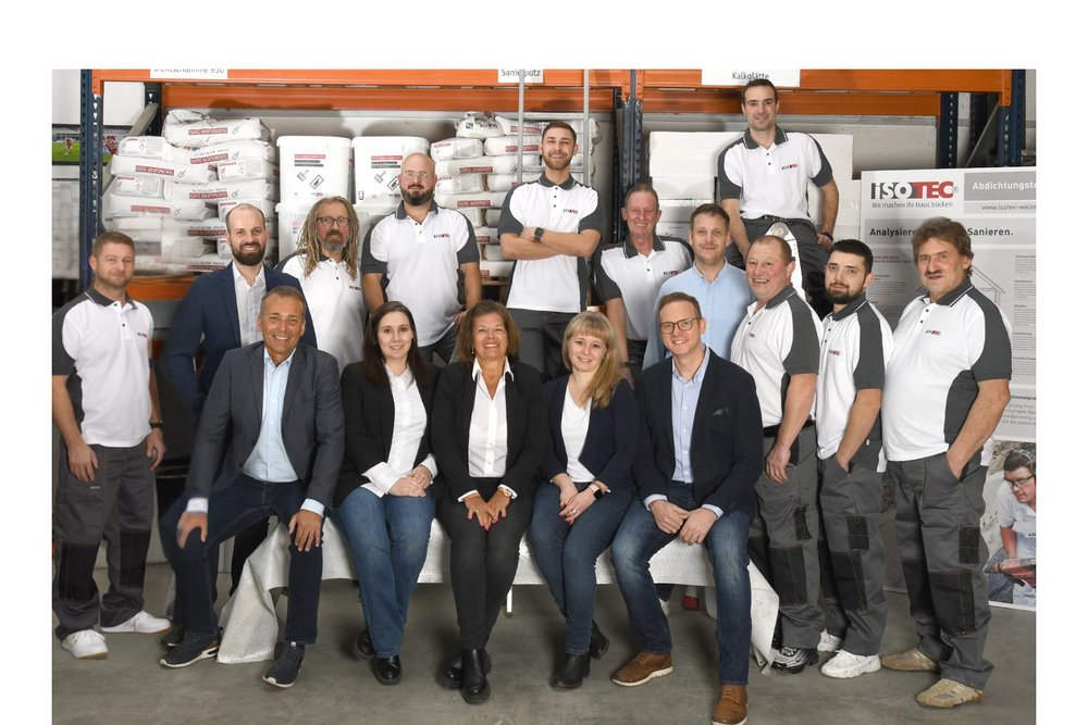ISOTEC Teamfoto in Lagerhalle mit Regalen, Säcken und Werkzeugen im Hintergrund