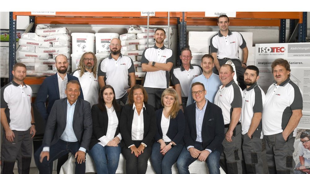 ISOTEC Teamfoto in Lagerhalle mit Regalen, Säcken und Werkzeugen im Hintergrund