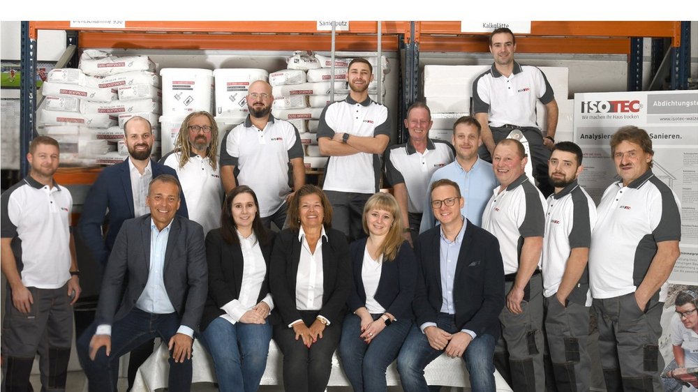 ISOTEC Teamfoto in Lagerhalle mit Regalen, Säcken und Werkzeugen im Hintergrund