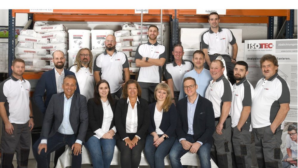 ISOTEC Teamfoto in Lagerhalle mit Regalen, Säcken und Werkzeugen im Hintergrund