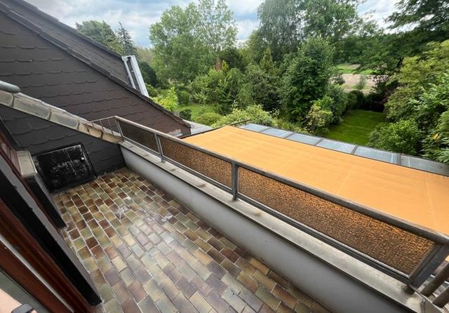 Balkon mit Fliesenboden, Sichtschutz und Blick in einen grünen Garten