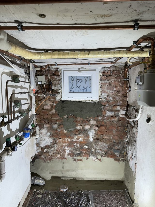 Freigelegte Ziegelwand im Keller mit grauer Masse unter kleinem Fenster