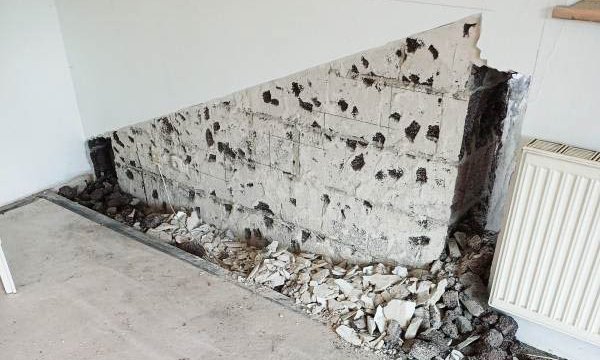 Freigelegte Mauerbasis mit schwarzen Flecken, Bauschutt am Boden neben Heizkörper.