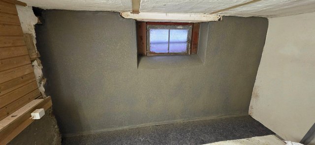 Kellerraum mit grauer Masse beschichteter Wand und kleinem Fenster.