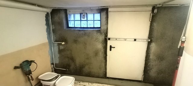 Dunkle Masse auf Kellerwand um Tür und Fenster