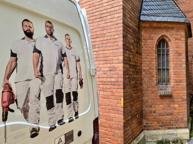 ISOTEC Mitarbeiter auf Transporter, daneben Backsteinfassade mit Spitzbogenfenster.