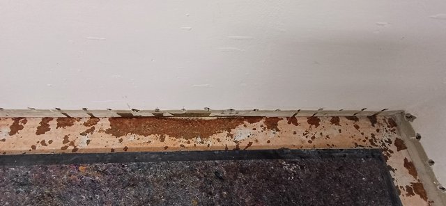 Abgeklebte Wandunterkante mit braunen Abplatzungen und grauer Schutzmatte am Boden