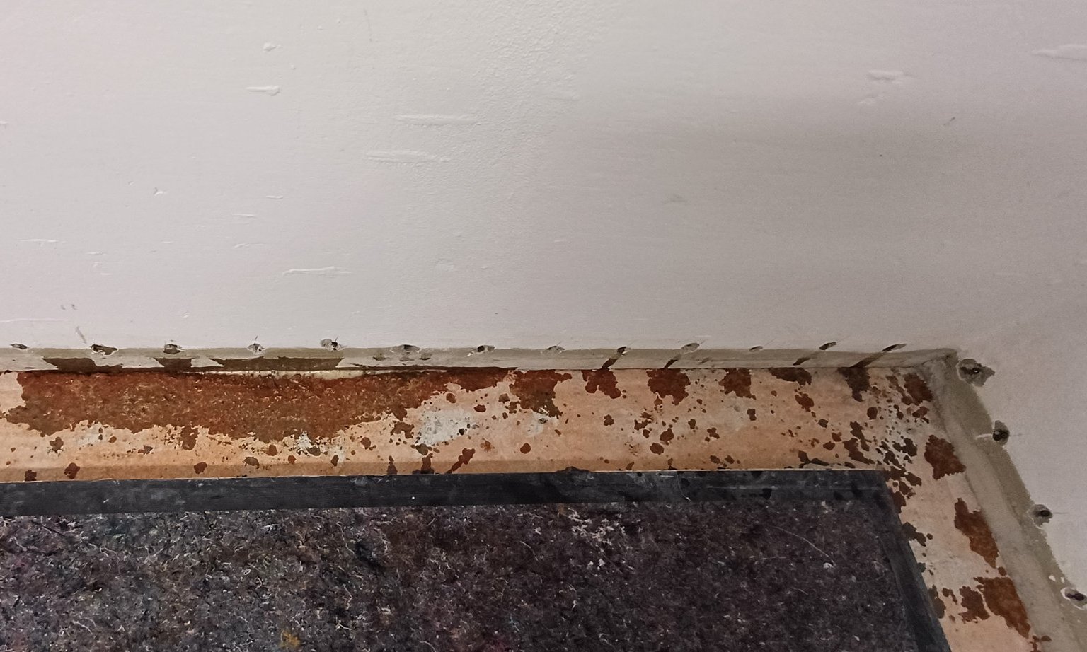 Abgeklebte Wandunterkante mit braunen Abplatzungen und grauer Schutzmatte am Boden