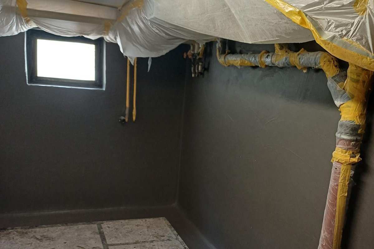 Abgeklebte Rohre unter Folienabdeckung in Kellerraum mit grauer Beschichtung