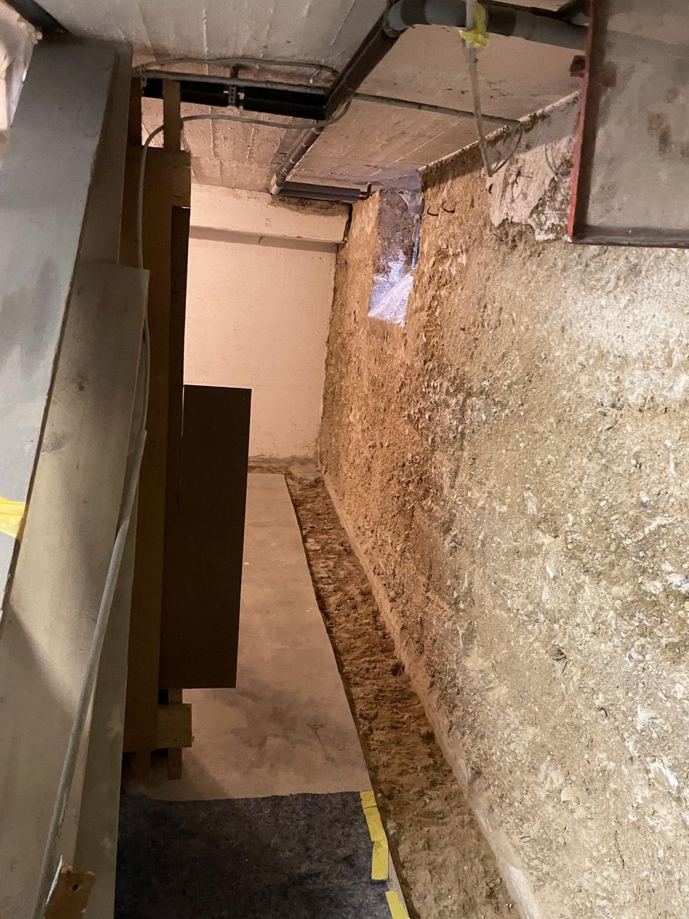 Schmaler Kellerbereich mit freigelegter Wand und Bodenrinne