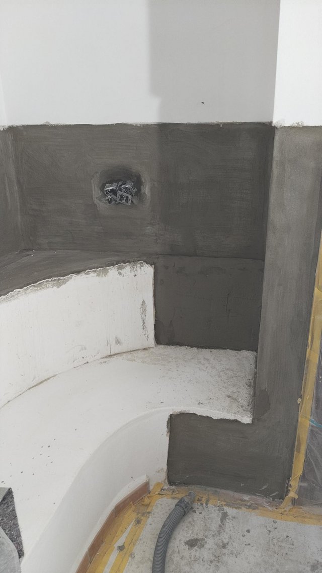 Graue Masse auf Wandbereich um Badewanne, freiliegende Elektroöffnung und abgeklebter Boden.