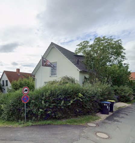 Wohnhaus mit Hecke, Baum und Fahne an einer Straßenecke