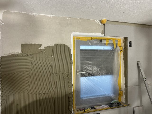 Tür mit Folie abgeklebt, graue Masse mit Rillen auf Wandfläche.