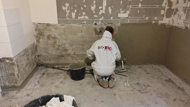 ISOTEC Mitarbeiter trägt graue Masse auf Wand im Raum auf.