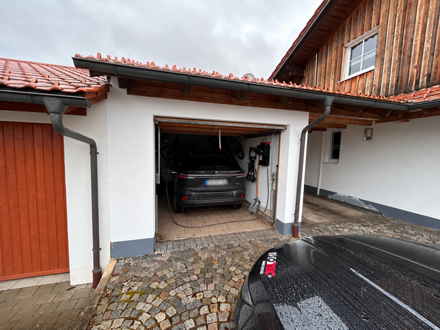 Offene Garage an Wohnhaus mit geparktem Auto und nassem Pflaster