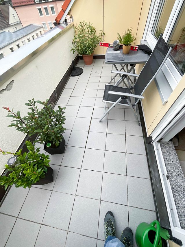 Schmaler Balkon mit grauen Bodenfliesen, Pflanzen, Tisch und zwei Stühlen