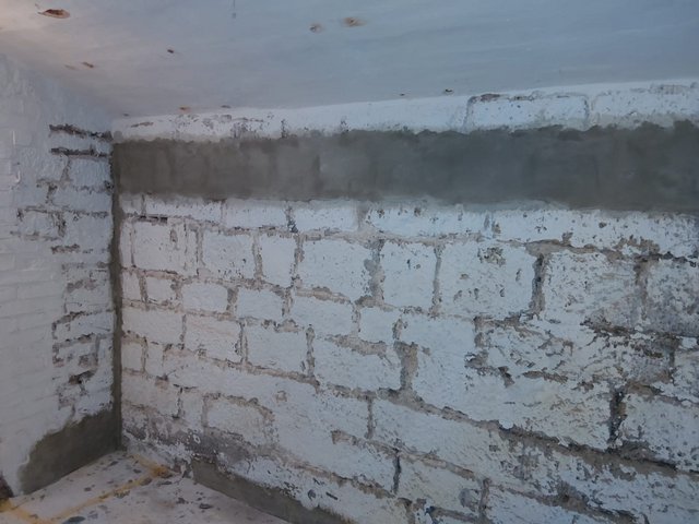 Weiße Ziegelwand im Keller mit aufgetragener grauer Masse im oberen Bereich