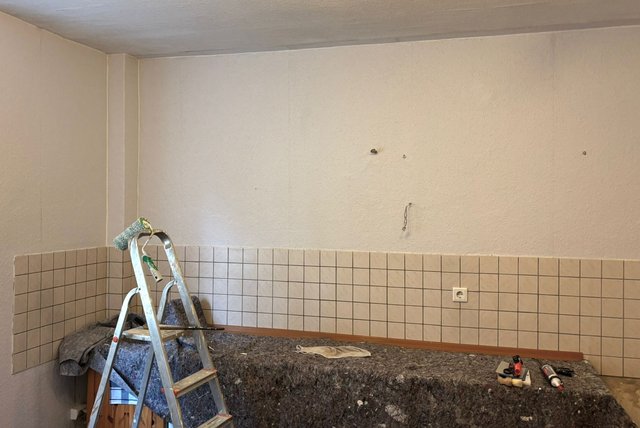 Leiter vor gefliester Zimmerwand mit Steckdose und freiliegendem Kabel