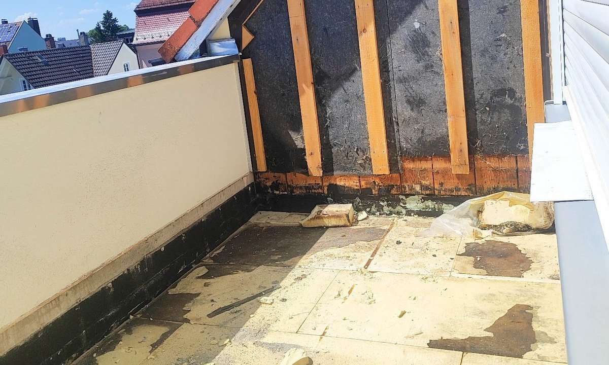 Freigelegte Dachgaube mit schwarzer Masse, Holzlatten und verschmutztem Balkonboden