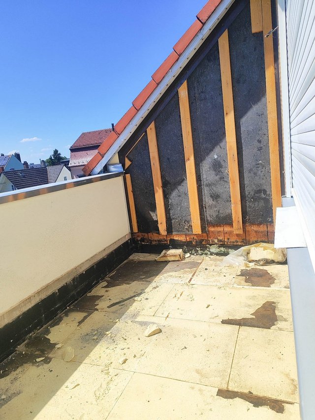 Freigelegte Dachgaube mit schwarzer Masse, Holzlatten und verschmutztem Balkonboden