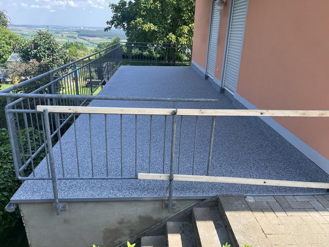 Balkon mit grauem Bodenbelag, Metallgeländer und Blick ins grüne Tal