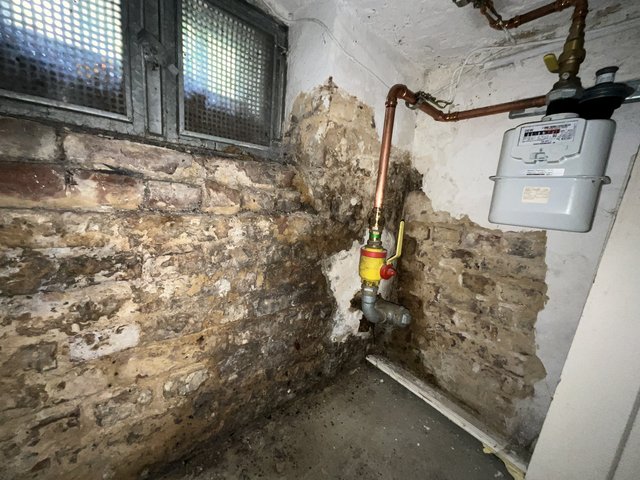 Feuchte, beschädigte Kellerwand mit sichtbaren Leitungen und Gaszähler