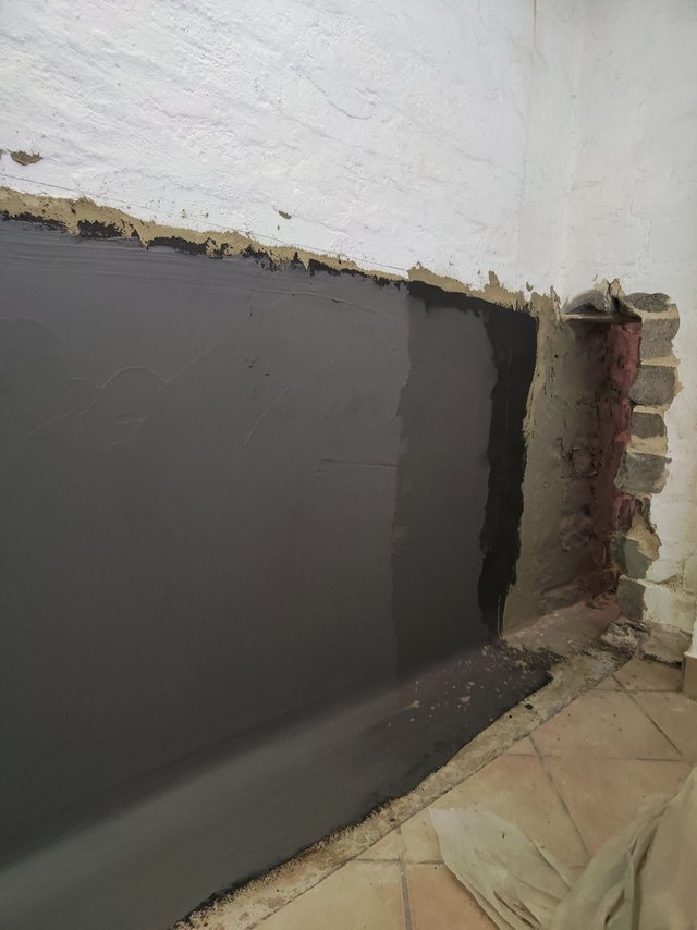 Schwarze Masse auf Wand neben freigelegtem Mauerwerk in Raumecke