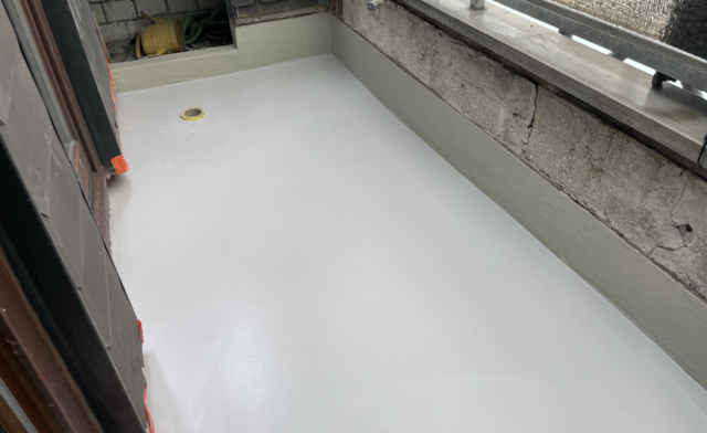 Heller Bodenbelag auf Balkon mit Ablauf und freigelegter Betonwand