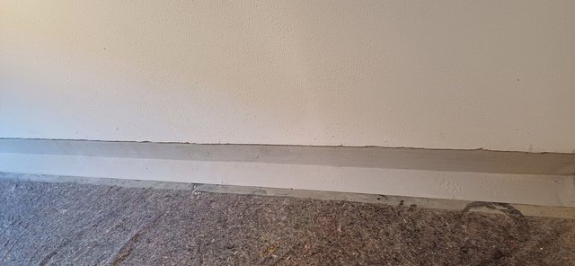 Graue Masse als horizontaler Streifen am Wandfuß, davor Filzabdeckung am Boden