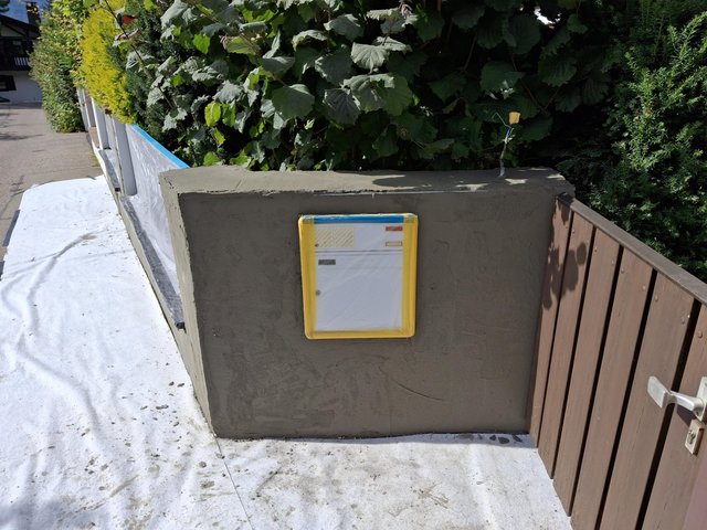 Niedrige Mauer mit grauer Masse und abgeklebtem Briefkasten.