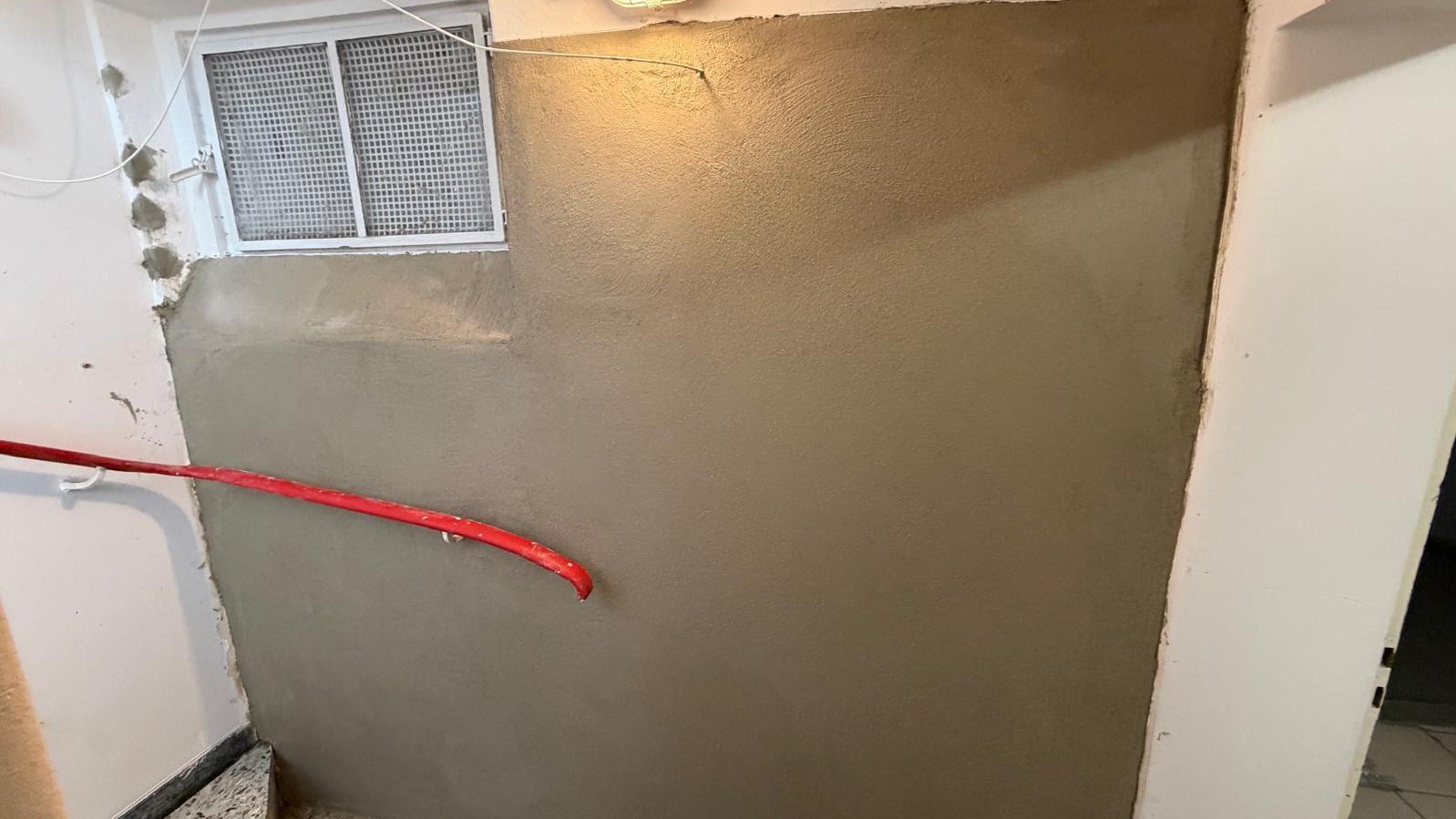 Graue Masse auf Kellerwand im Treppenbereich unter Fenster aufgetragen