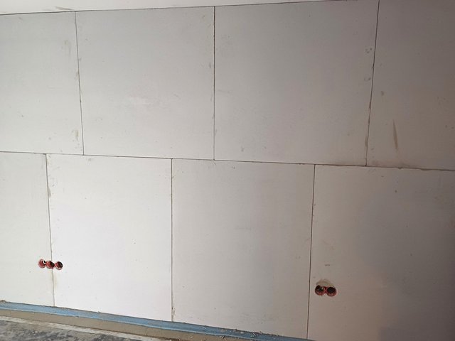 Weiße Platten an Wand verlegt, rote Leerrohre ragen aus dem unteren Wandbereich.