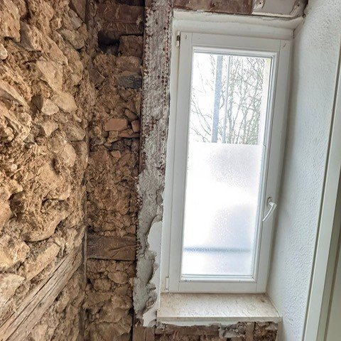 Freigelegte Bruchsteinwand neben schmalem Fenster im Innenraum