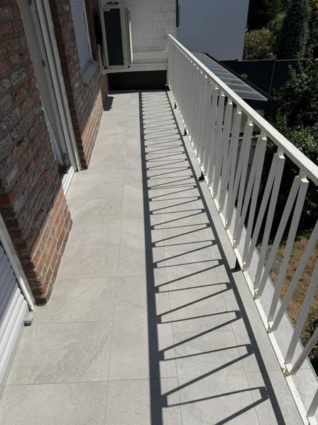 Schmaler Balkon mit hellen Fliesen und weißem Geländer im Sonnenlicht