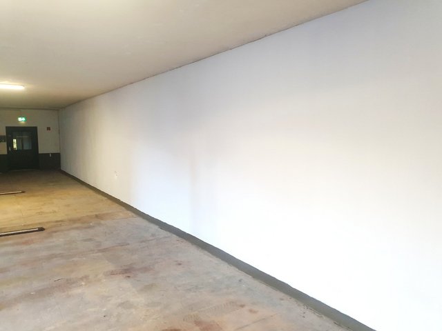 Langer Flur mit glatter weißer Wand und grauem Bodenrand