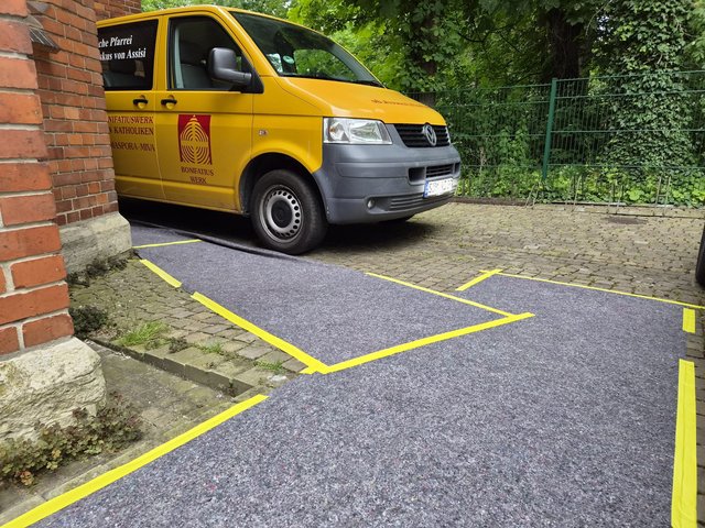 Gelber Transporter neben Backsteinwand, Filzbahn mit gelbem Klebeband markiert