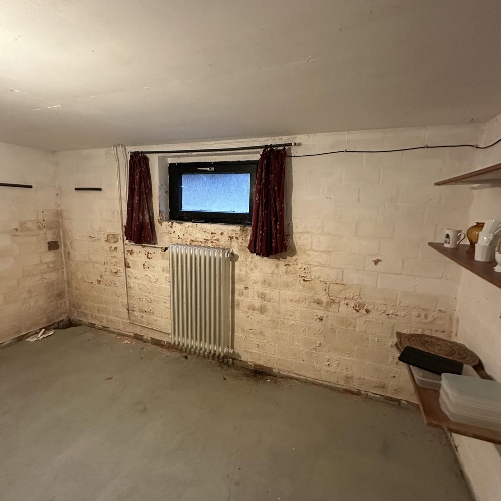 Kellerraum mit verfärbter Ziegelwand, kleinem Fenster und Heizkörper