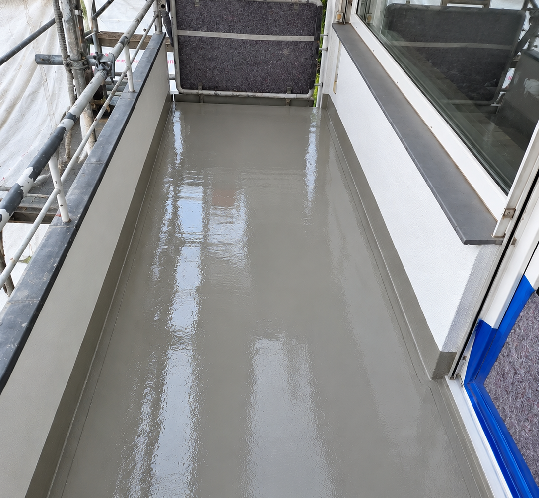 Balkon mit frisch aufgetragener, glänzender grauer Masse auf dem Boden, Gerüst im Hintergrund